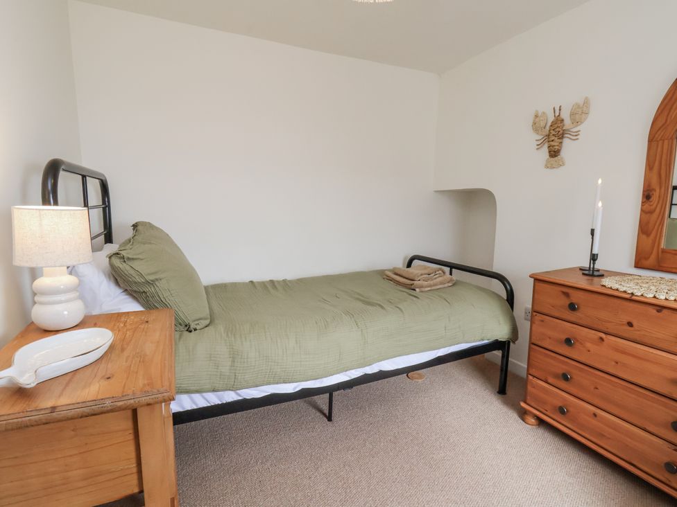 A bedroom with a bed, lamp, dresser and towels at Launcher's Cottage in Scarborough