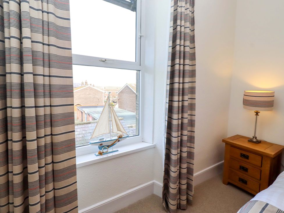 A bedroom with curtains, window, lamp, and model sailboat at Dinguardi in Seahouses