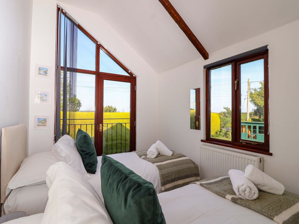 A bedroom with two beds and windows showing green fields at 1 Eastdon Cottages in Exeter
