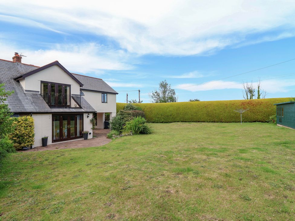 A garden with a house and hedge at 1 Eastdon Cottages in Exeter