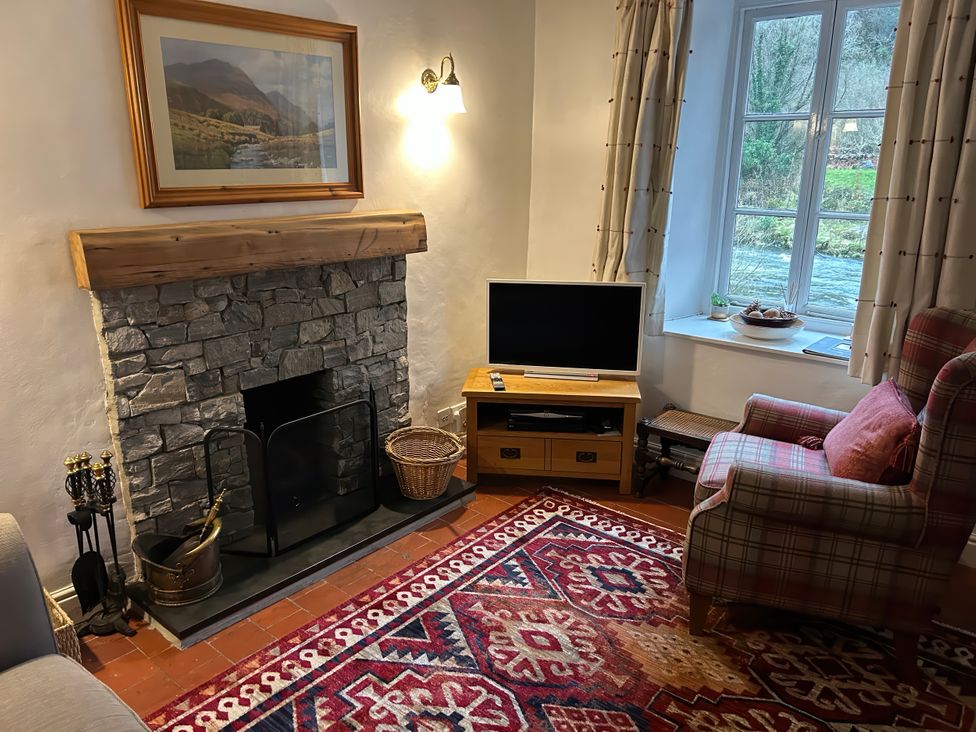 A living room with a fireplace and television at Riverbank Cottage in Beddgelert