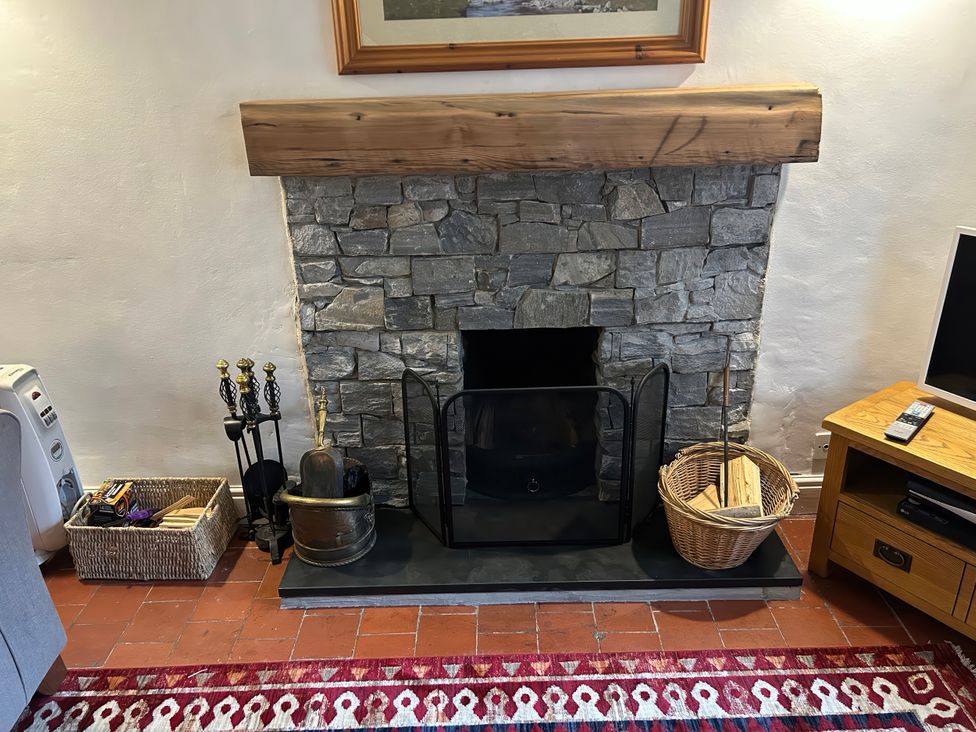 A fireplace with stone surround and firewood basket at Riverbank Cottage in Beddgelert