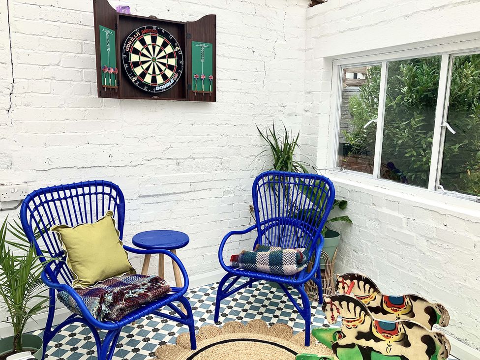 A snug area with two blue chairs, a dartboard, and a small table at Derwen House, Llangollen