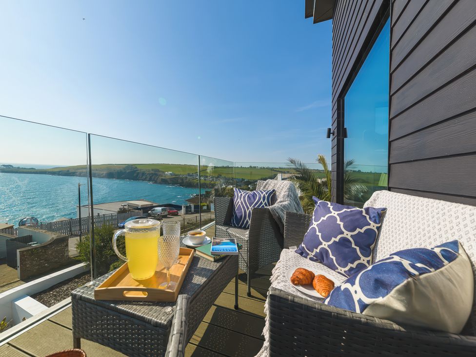 A balcony with wicker chairs cups books and a pitcher of lemonade overlooking the sea at Oystercatcher in Mevagissey