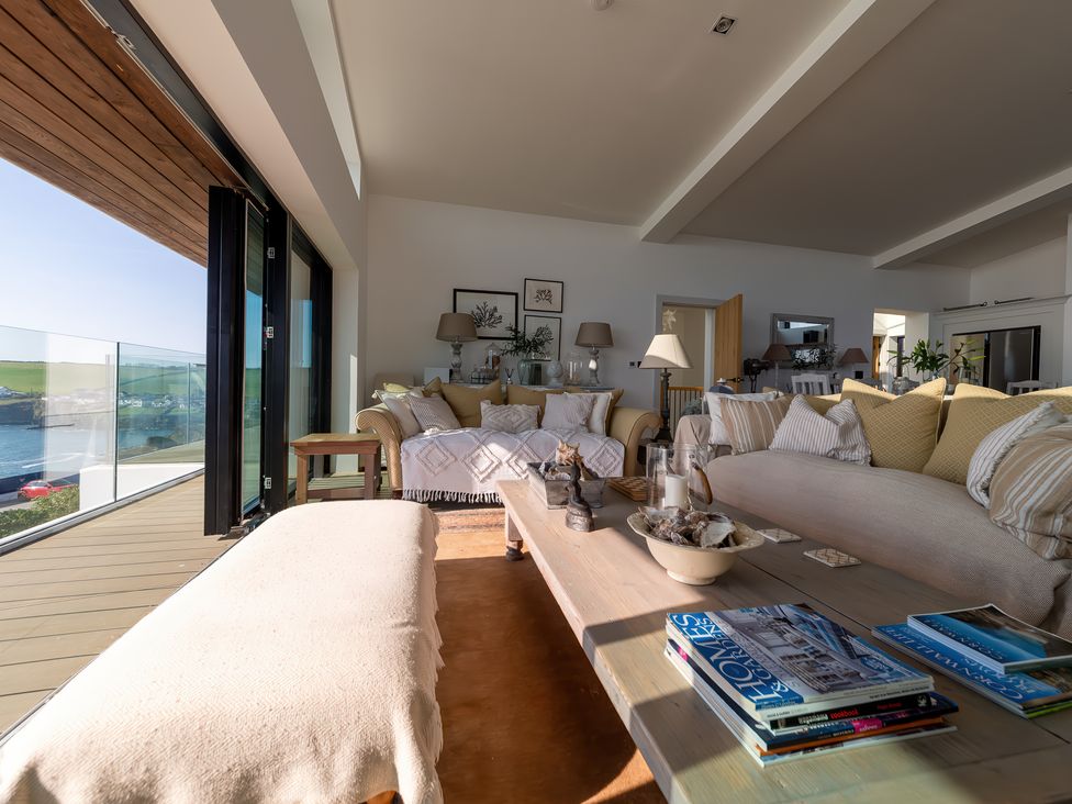 A living room with sofas cushions coffee table and glass doors overlooking a coastal view at Oystercatcher in Mevagissey