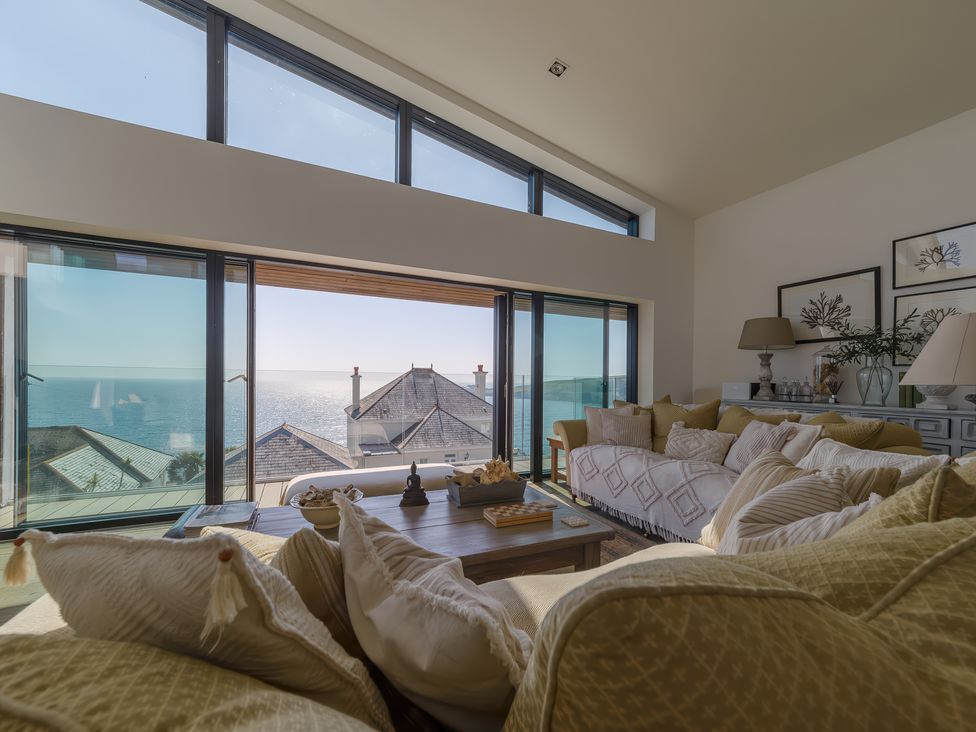 A living room with couches coffee table lamps and framed pictures with ocean view at Oystercatcher in Mevagissey