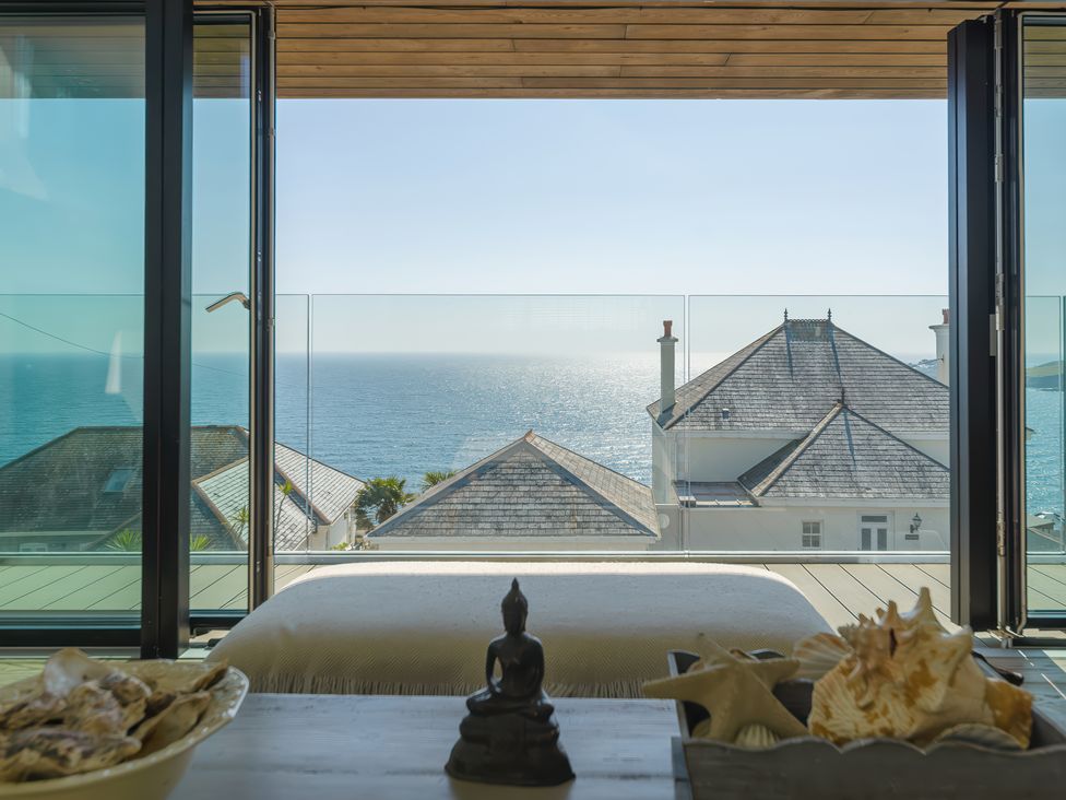 A room with a bed and decorative shells on a table with a sea view through glass doors at Oystercatcher in Mevagissey