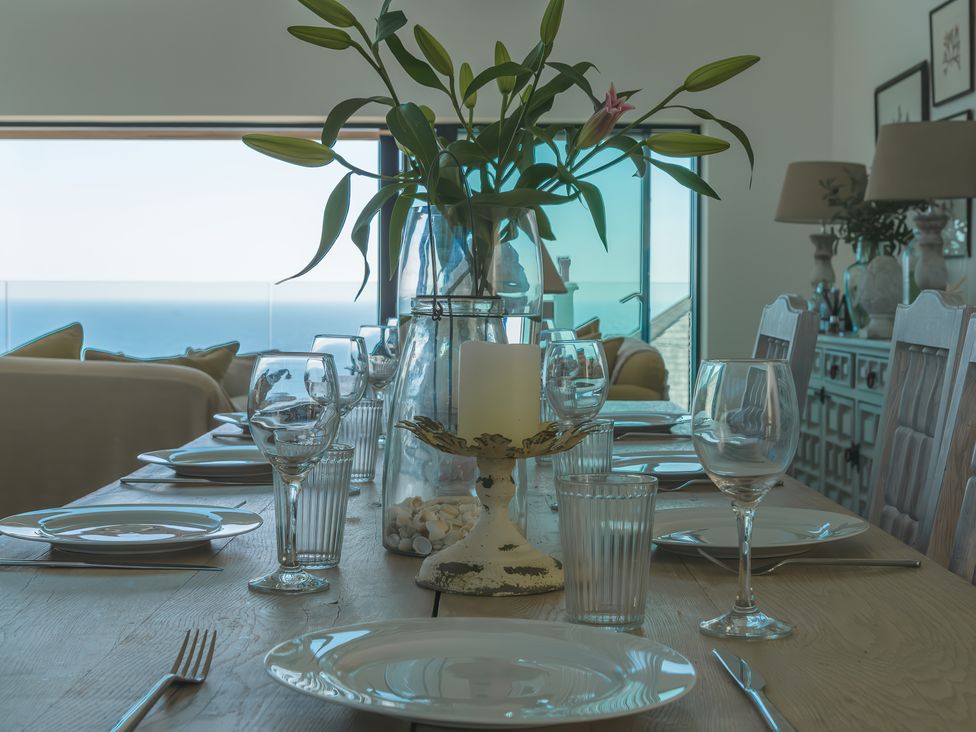 A dining table set with plates glasses and cutlery with a vase of flowers and a candle holder at Oystercatcher in Mevagissey