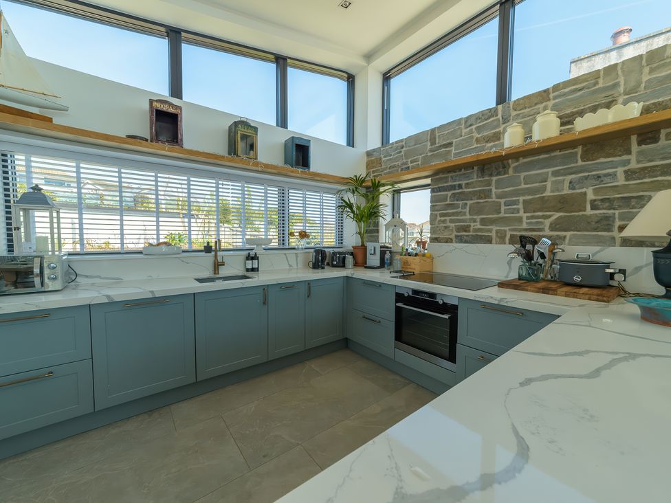 A kitchen with blue cabinets stone wall and large windows at Oystercatcher in Mevagissey