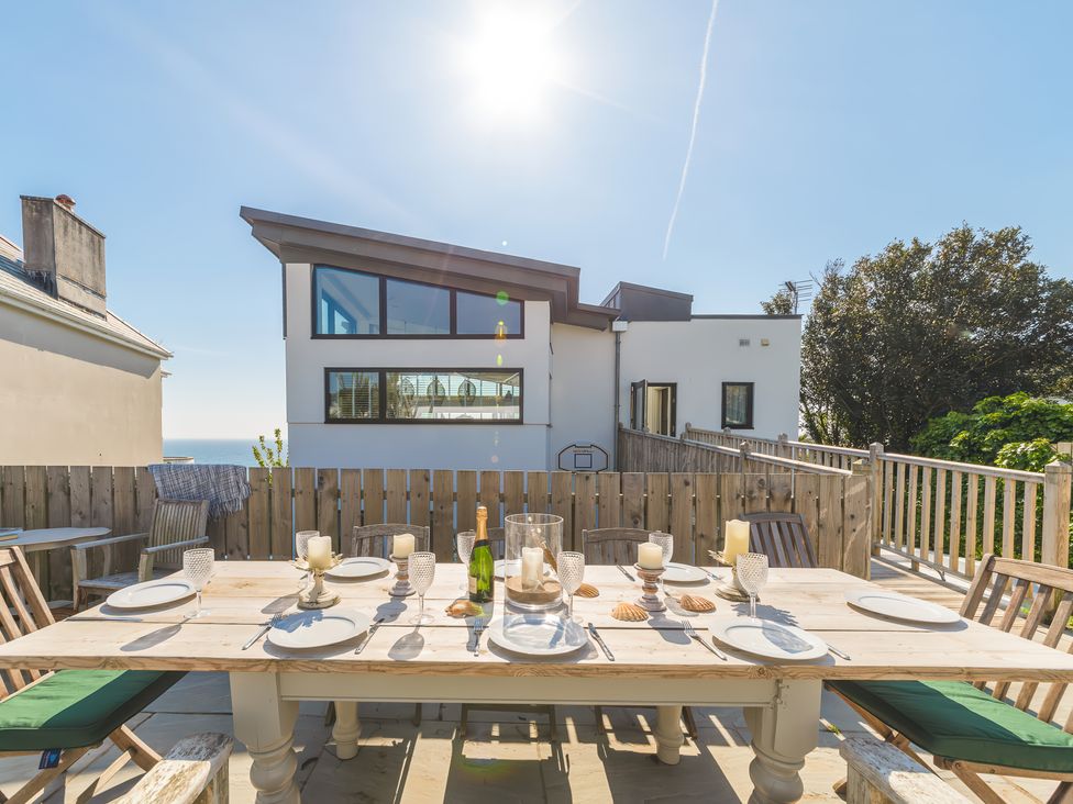 An outdoor dining table set with plates glasses candles and a bottle on a deck with wooden fence and modern houses in the background at Oystercatcher in Mevagissey