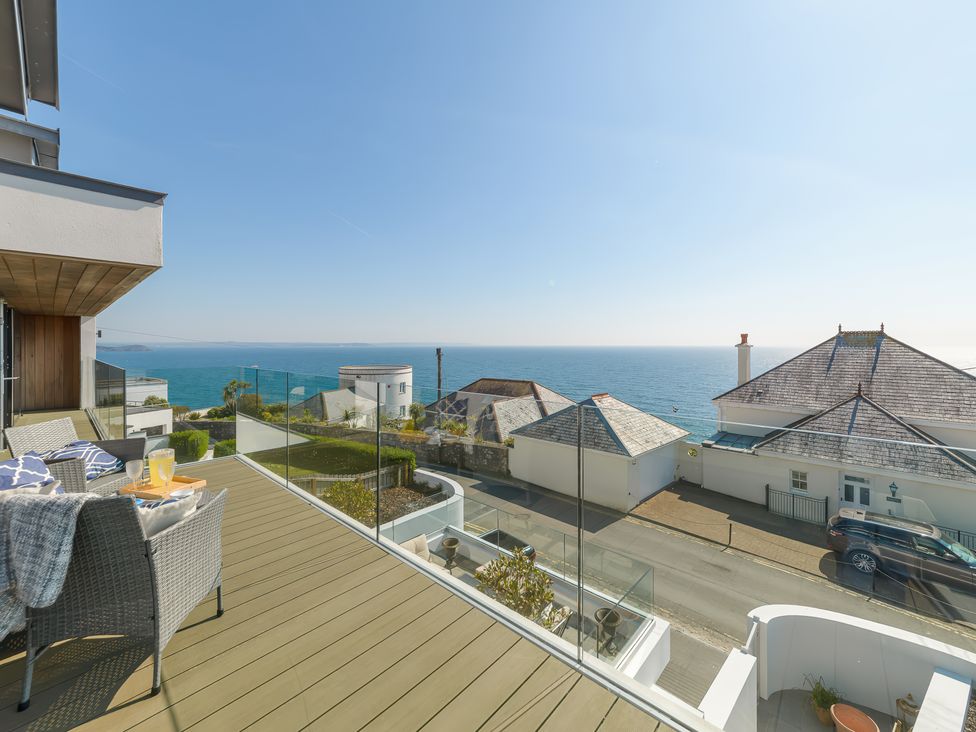 A balcony with wicker chairs and glass railing overlooking the sea and neighboring houses at Oystercatcher in Mevagissey