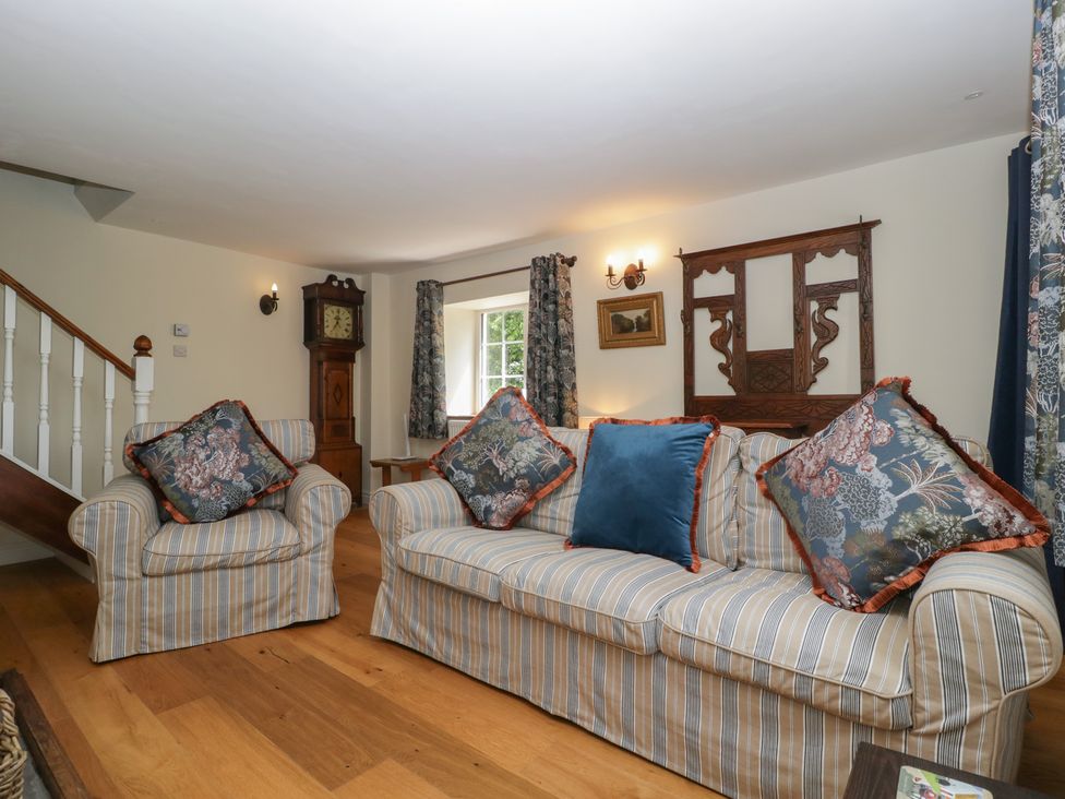 A living room with a sofa, armchair, and wall clock at Court House Cottage in Gatcombe near Blakeney