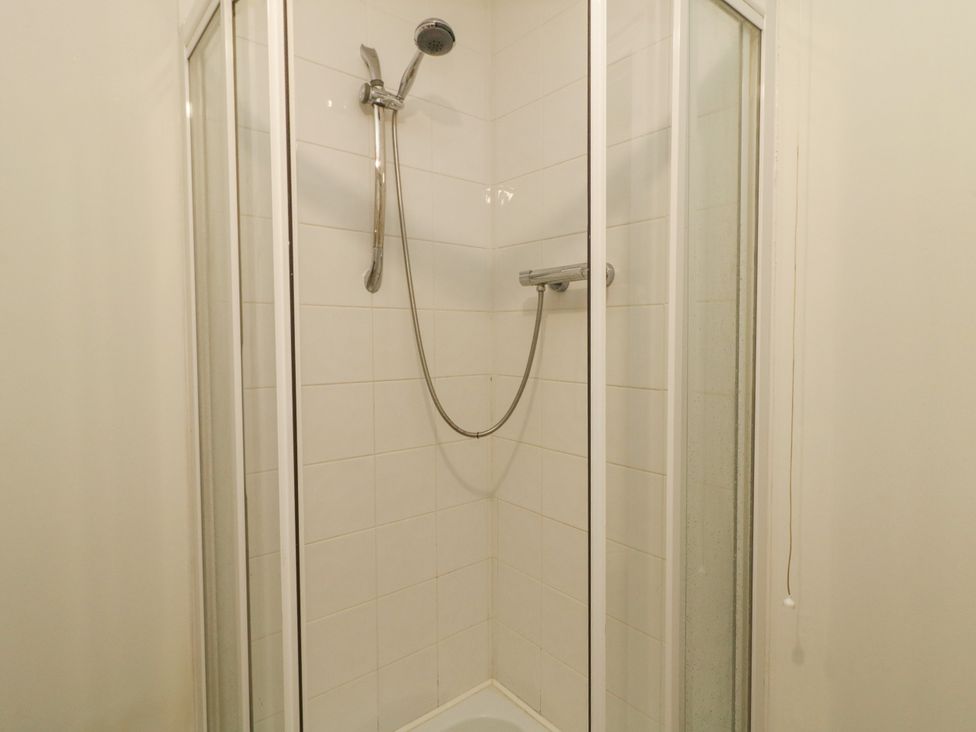 A shower with glass doors and tiles at Woodside Guest House in Castlerock
