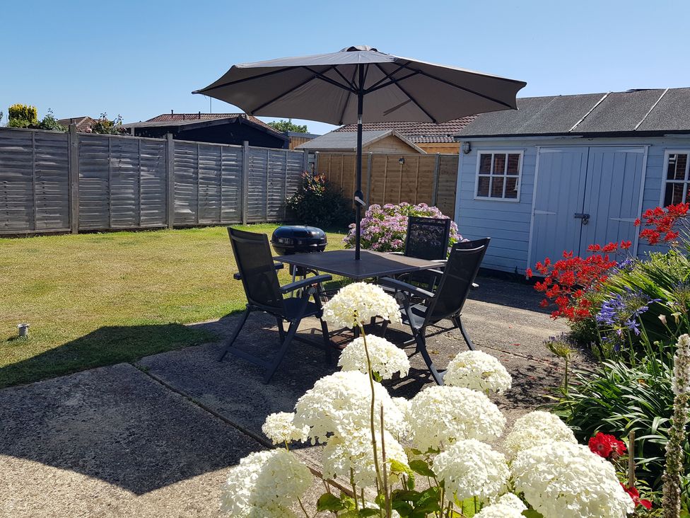A garden with a table and chairs under an umbrella at Seafarer's Rest in Selsey