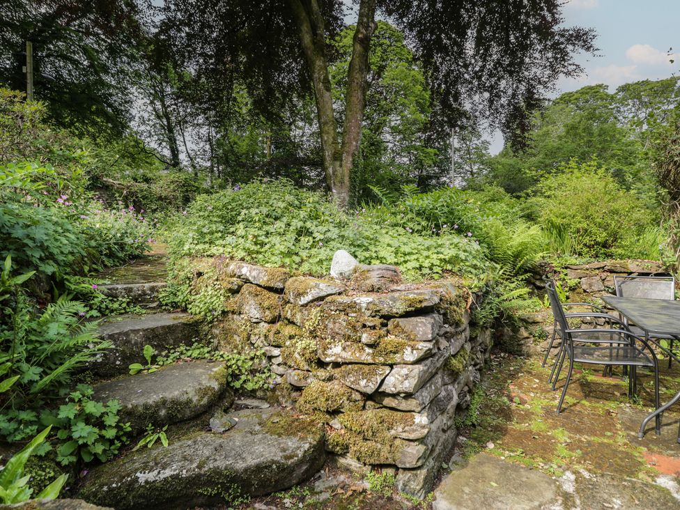 A garden with stone steps, a wall, and a table with chairs at Glandwr Cottage Llanbedr