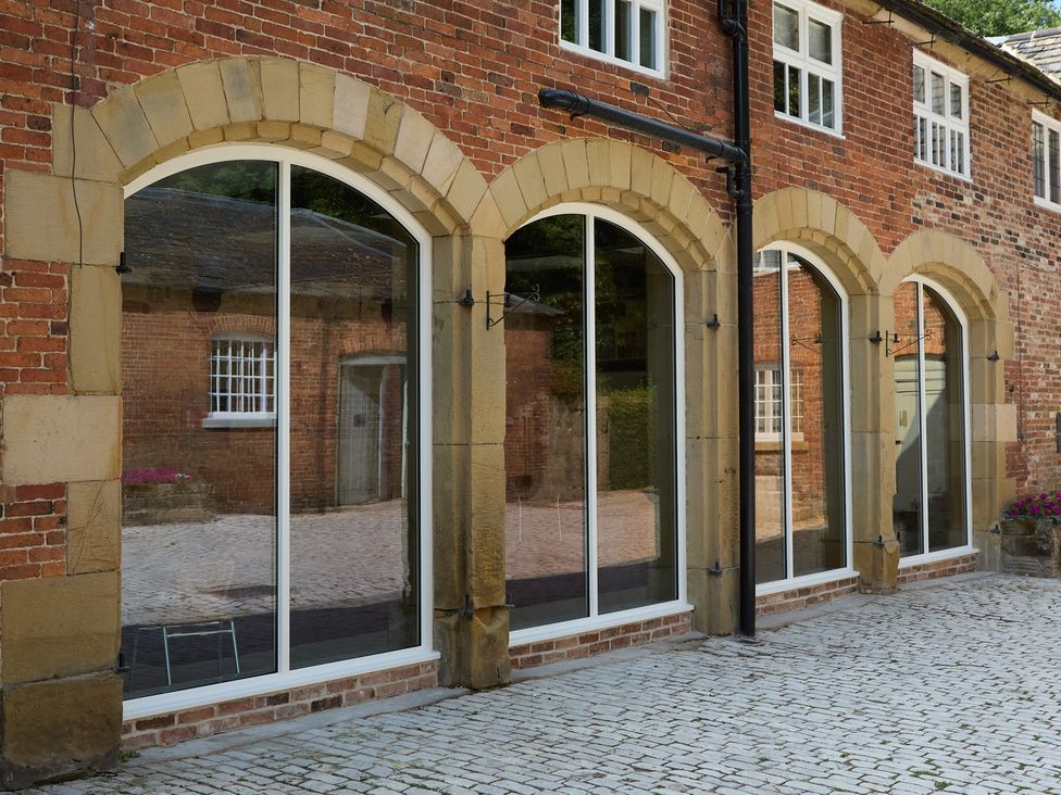 An outdoor view of large windows with stone arches and a cobblestone pathway at The Card House in Hopton