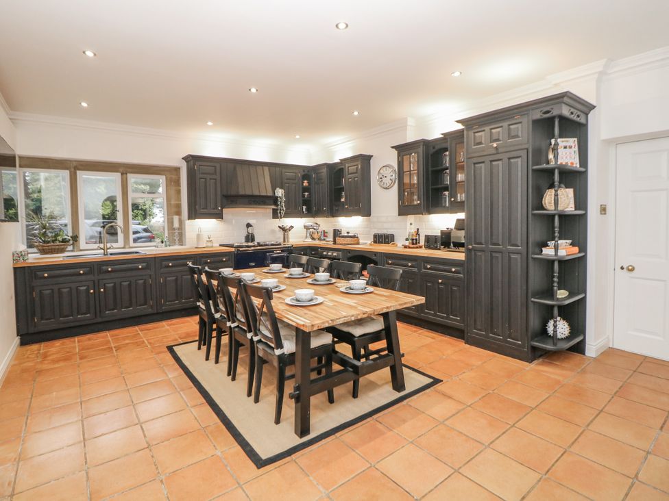 A kitchen with dark cabinets and a wooden dining table at Hallfield Hall Cottage in Shirland