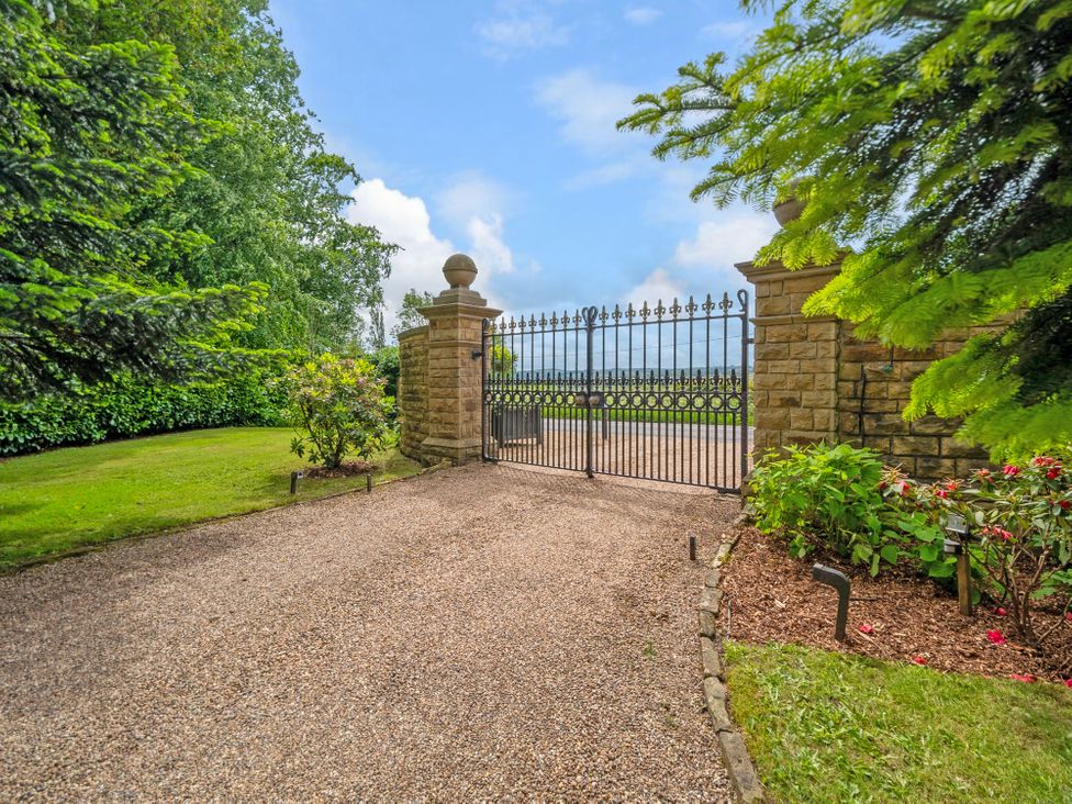 A gated entrance with gravel pathway and surrounding greenery at Hallfield Hall Cottage in Shirland