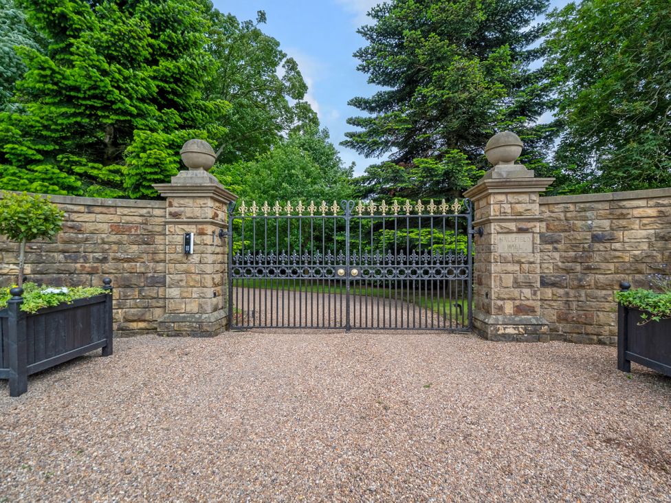 A gated entrance with stone pillars and greenery at Hallfield Hall Cottage in Shirland