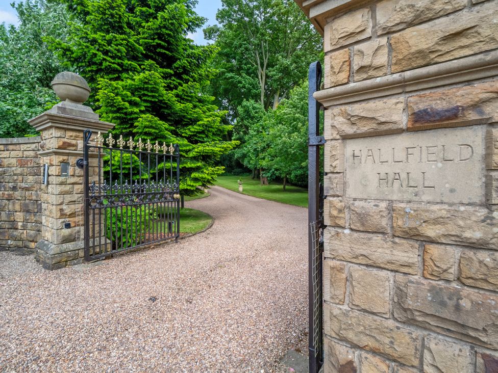A gated entrance with a stone wall and trees at Hallfield Hall Cottage Shirland