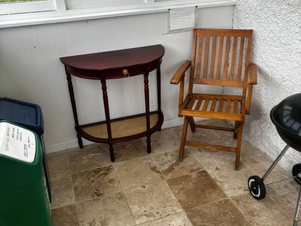 A table and chair with a recycling bin and barbecue grill at Strathnoon in Clune near Carrbridge