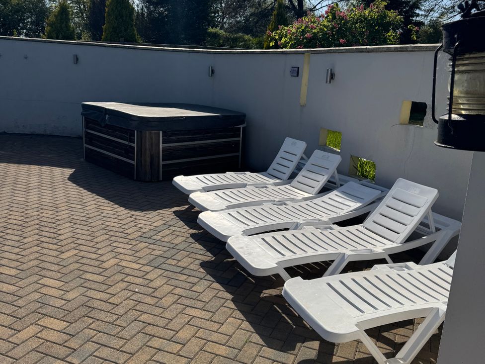 An outdoor patio area with four white lounge chairs and a covered hot tub against a white wall at Cuddfan in Llanteg