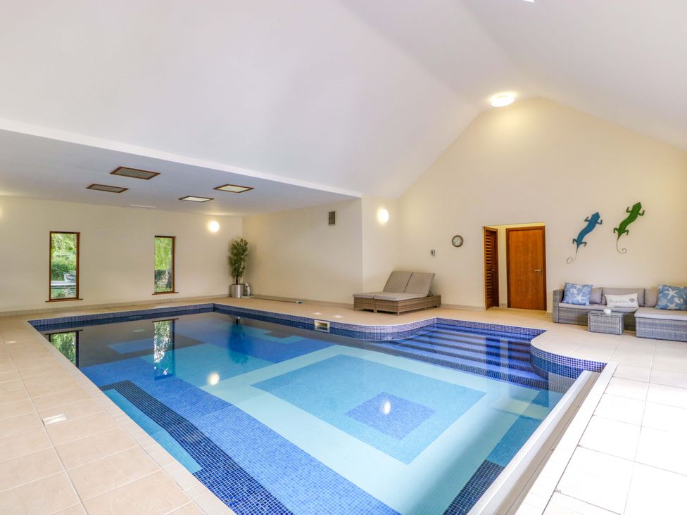 An indoor pool area with loungers and a sofa at Heathcliffe House in Castleton near Cardiff