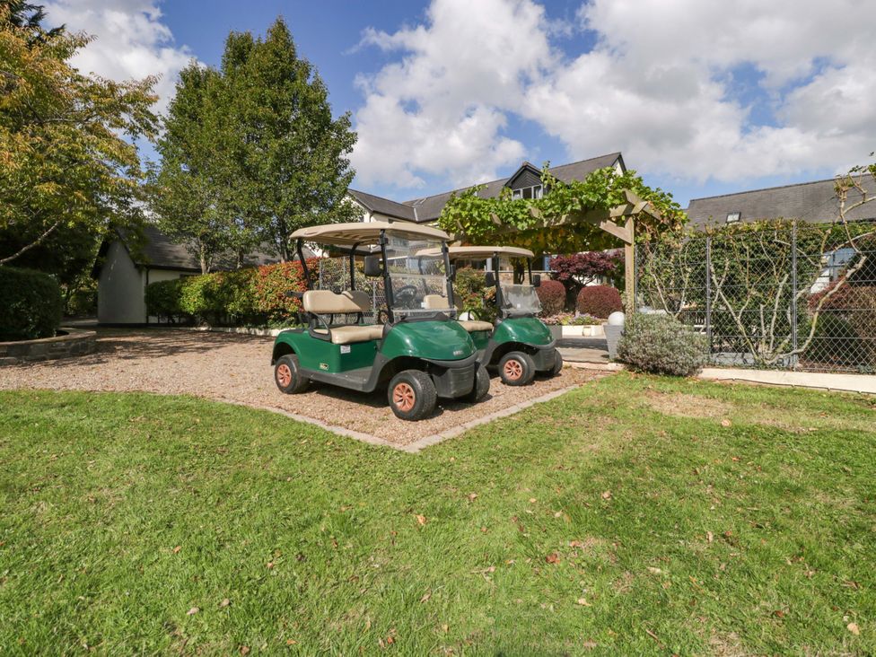 Two golf carts parked on gravel with trees and a building at Heathcliffe House in Castleton near Cardiff