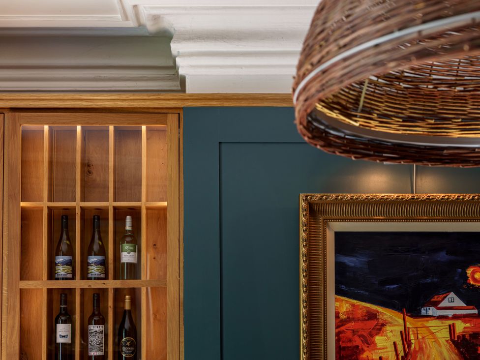A wine cellar with wine bottles in a wooden cabinet and a framed painting at Leathes Head Country House Borrowdale near Keswick
