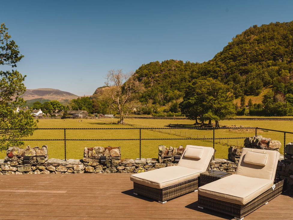 A deck with sun loungers overlooking a grassy field and mountains at Leathes Head Country House Borrowdale near Keswick