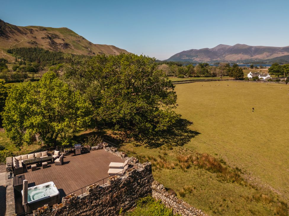 An outdoor deck with seating, a hot tub, and a barbecue grill overlooking a grassy field with trees and hills in the background at Leathes Head Country House Borrowdale near Keswick