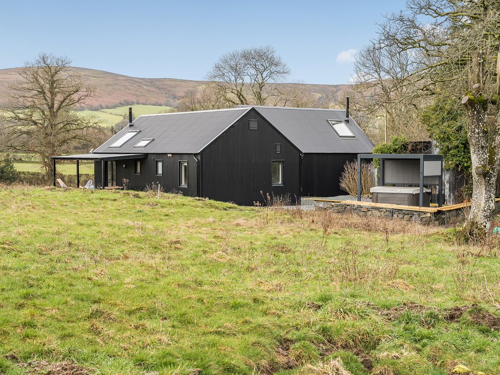 A house with a deck and hot tub on grass at Grove Cottage in Kington