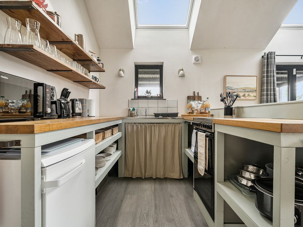 A kitchen with shelves, stove, and sink at Grove Cottage, Kington