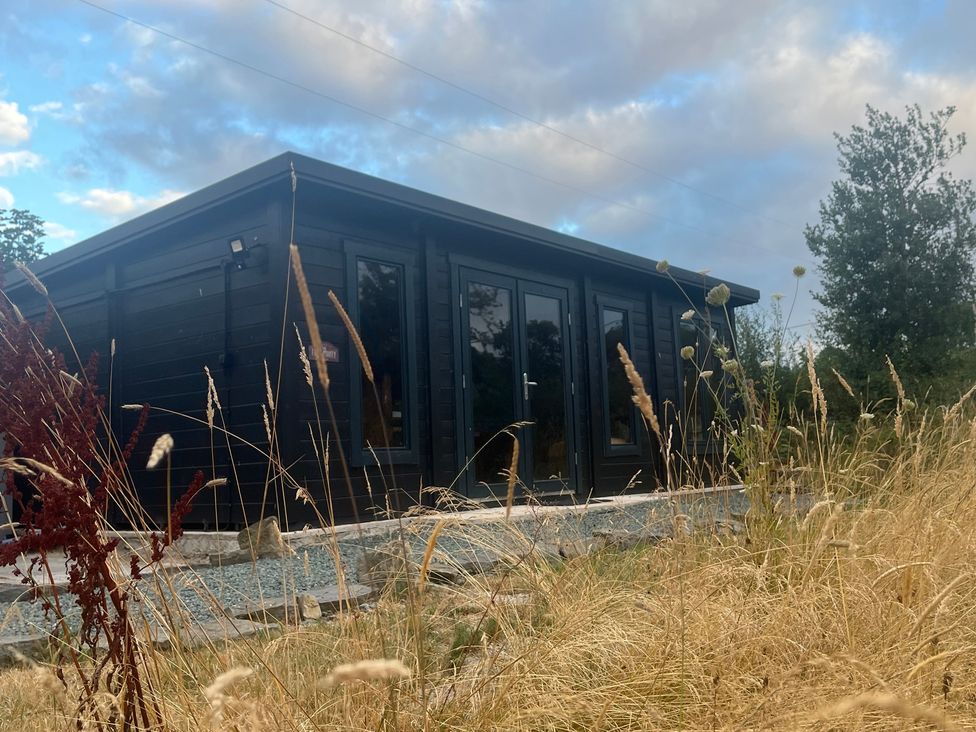 A cabin with windows and door surrounded by grass at Grove Cottage in Gladestry