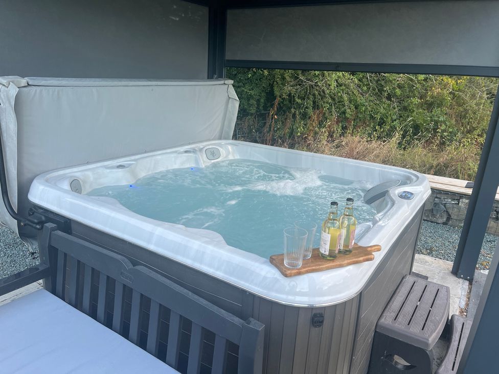 A hot tub with bottles and glasses on a table in the outdoor area at Grove Cottage in Gladestry