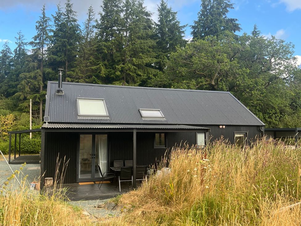 A black building with a deck and chairs at Grove Cottage in Gladestry