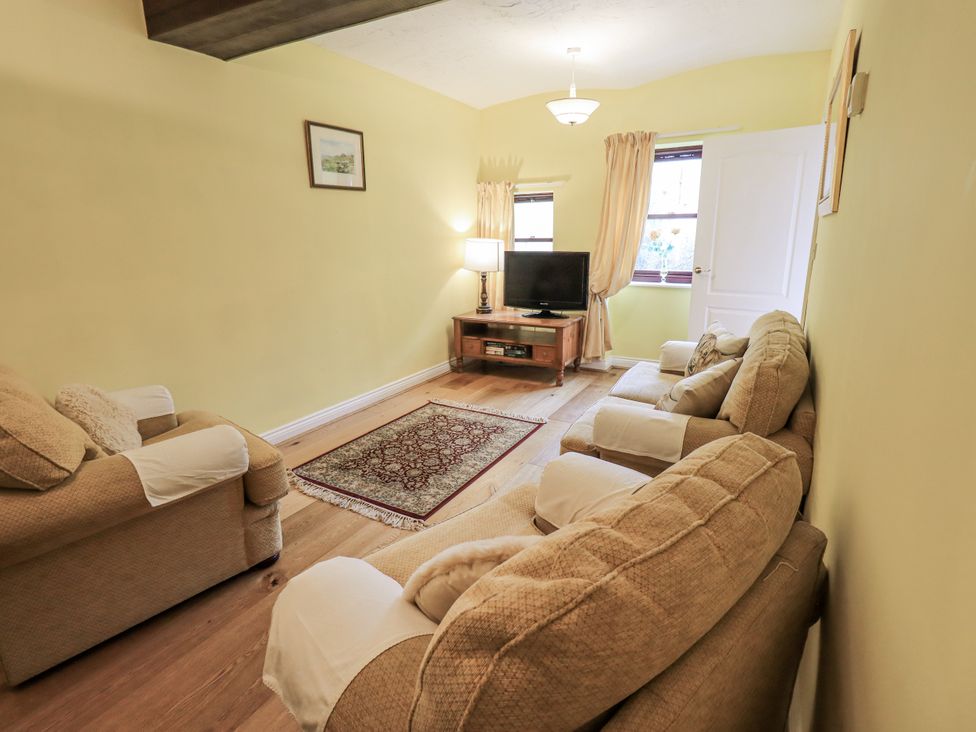 A living room with a sofa, television, and rug at Millers Cottage in Seaville near Wigton