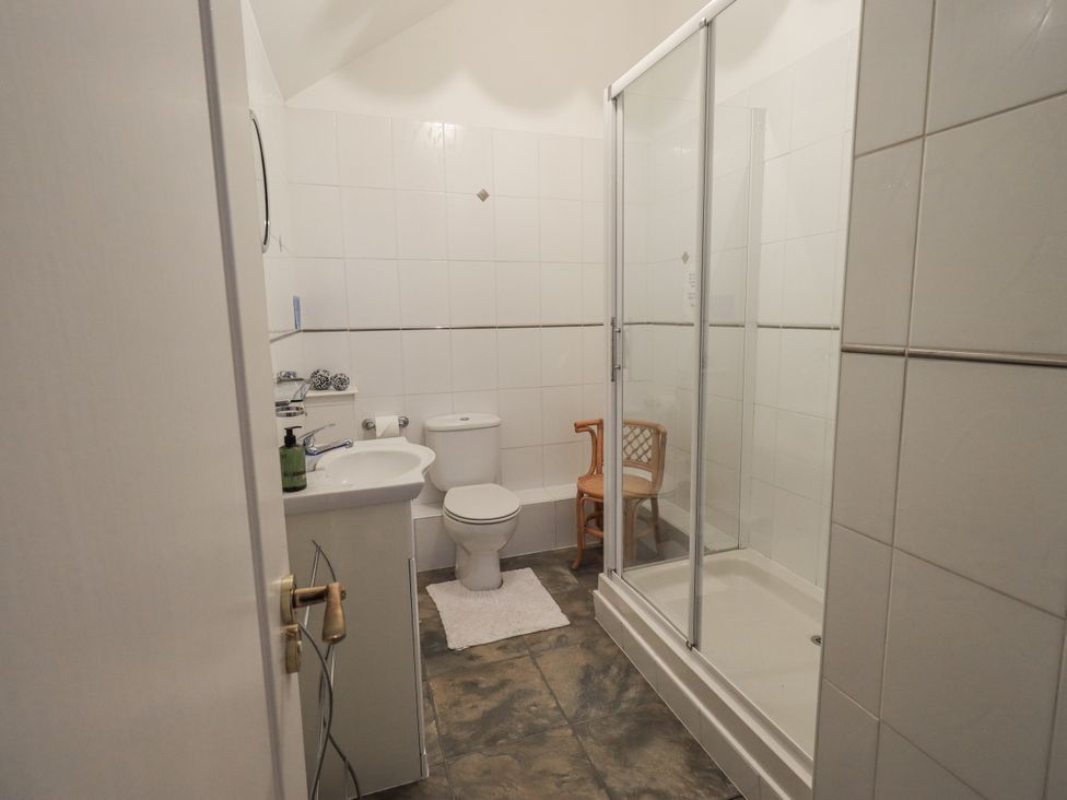 A bathroom with a shower, sink, toilet, and chair at Millers Cottage Seaville near Wigton