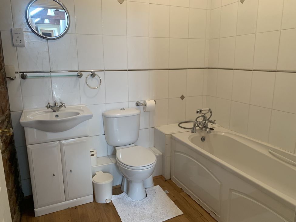 A bathroom with a bath tub, toilet, sink, and mirror at The Hayloft near Wigton