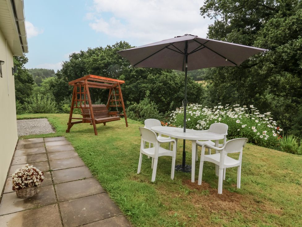 A garden with a table, chairs, and a swing at Hideaway in Great Torrington