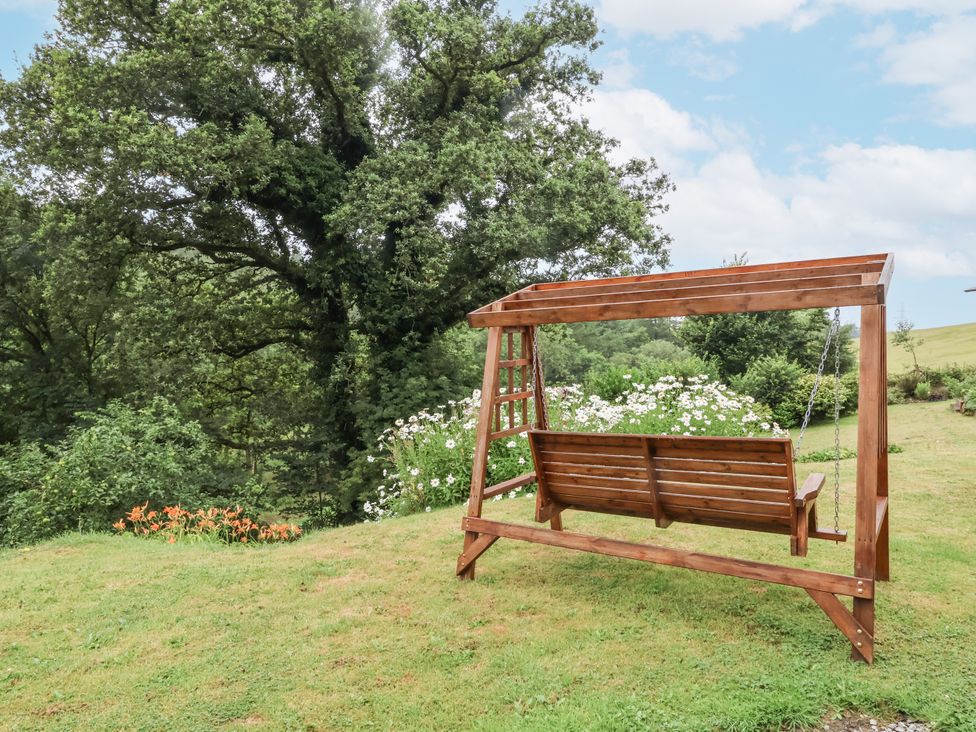 A swing in a garden with trees and flowers at Hideaway in Great Torrington