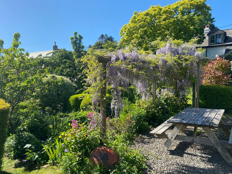 A garden with a wooden pergola covered in flowering vines and a wooden picnic table at Magnolia View in Goodleigh near Barnstaple