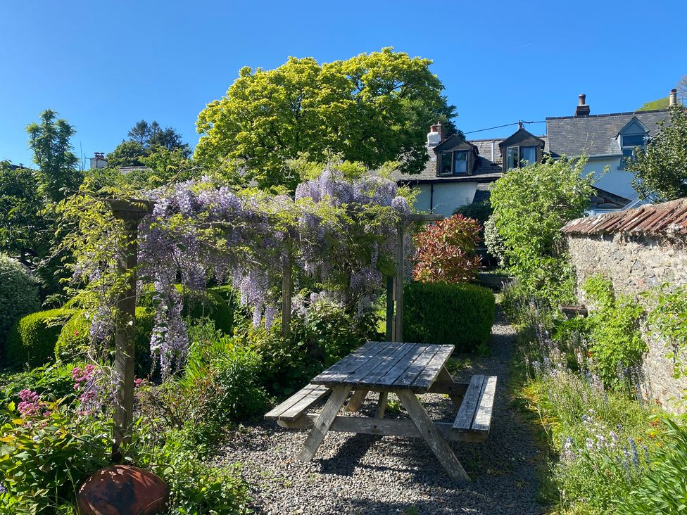 A garden with a wooden picnic table under a pergola covered in wisteria near a stone wall at Magnolia View in Goodleigh near Barnstaple