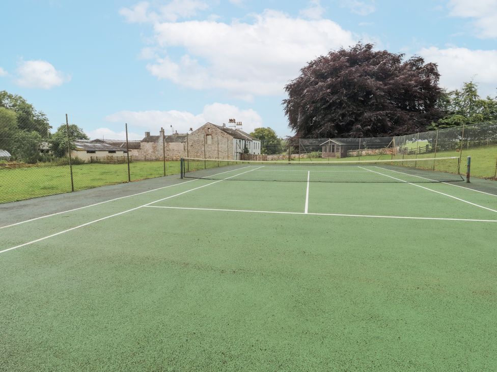 A tennis court with a net and buildings in the background at Westward Park near Wigton