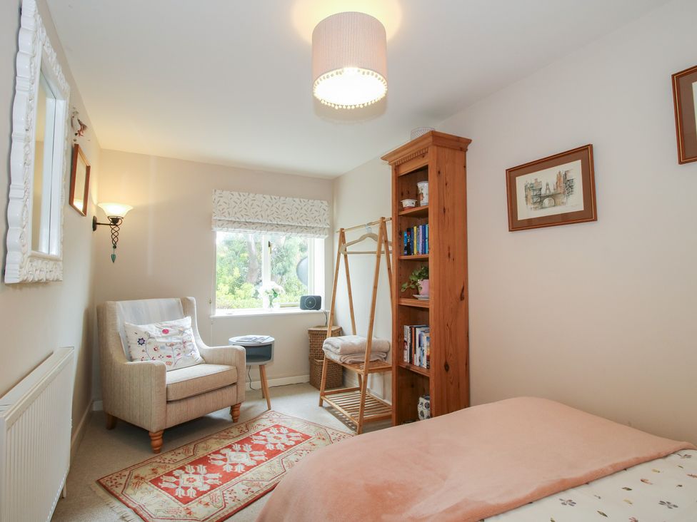 A bedroom with a bed, armchair, and bookshelf at Heribert Cottage in Shrewsbury