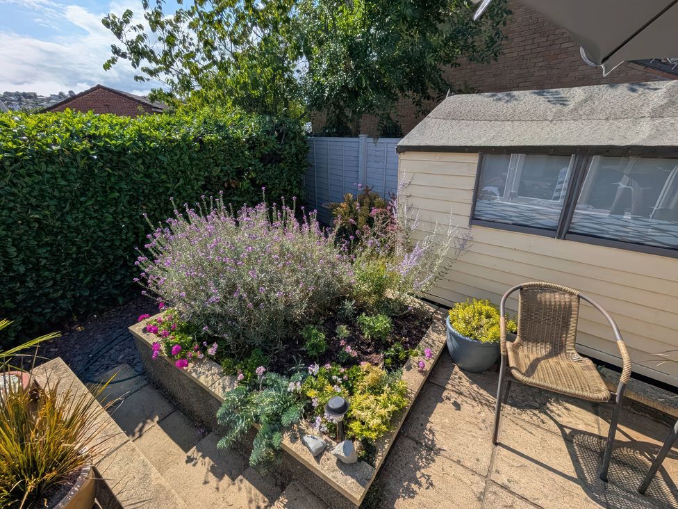 A garden with a flower bed, wooden shed, and a chair at Seahills Lyme Regis
