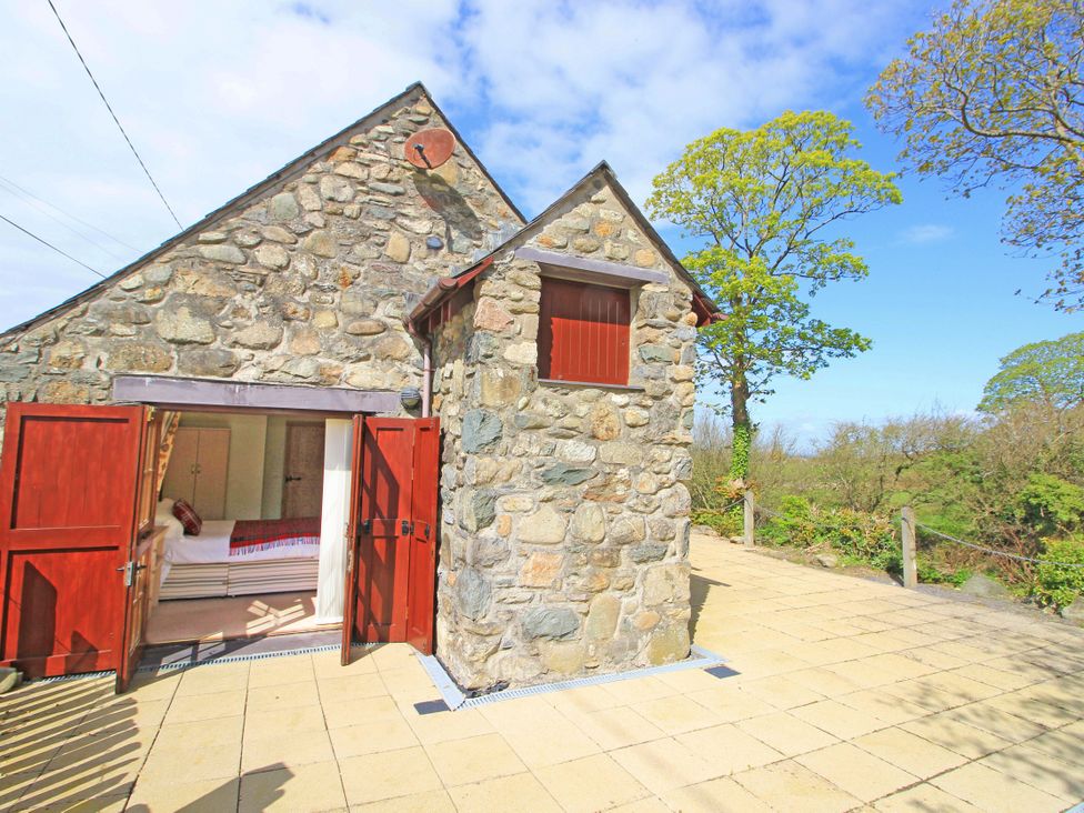 An outdoor patio with stone walls and red wooden doors leading to a bedroom at Melin Y Cim in Caernarfon
