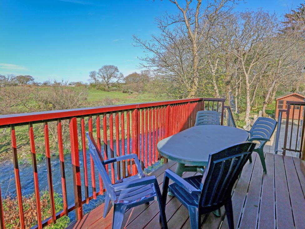 An outdoor deck with a table and four chairs overlooking a river and trees at Melin Y Cim in Caernarfon