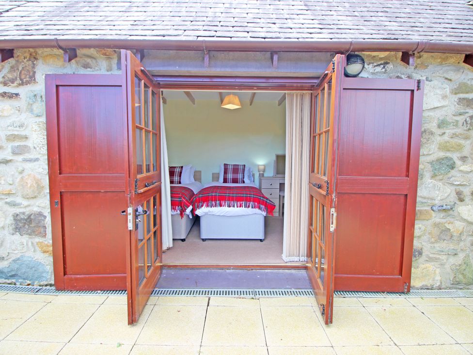 A bedroom with two single beds with red plaid blankets viewed through open wooden double doors at Melin Y Cim in Caernarfon