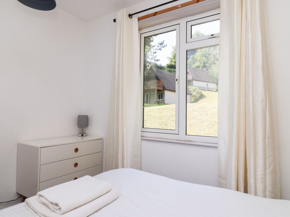 A bedroom with a window, dresser, lamp, and towel at Valley Lodge 37 St Ann's Chapel, Cornwall